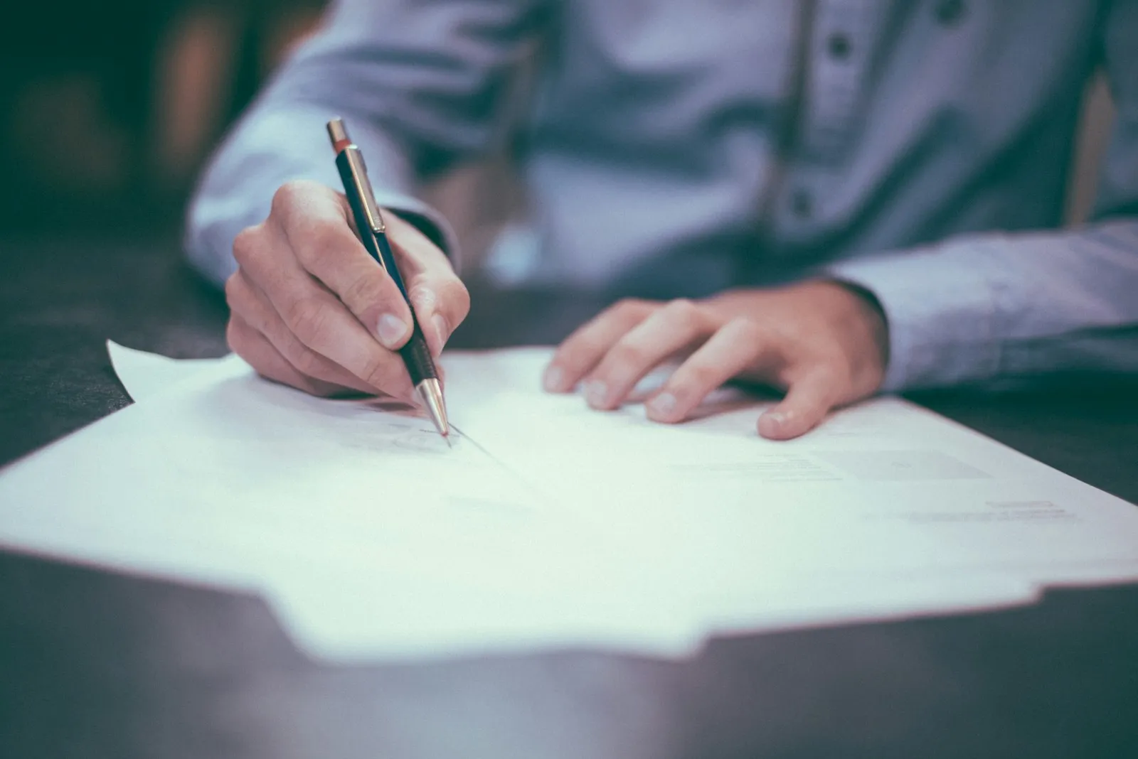 Pessoa assinando documentos sobre a mesa com uma caneta